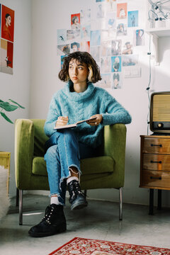 Trendy pensive teenager taking notes in diary while chilling at