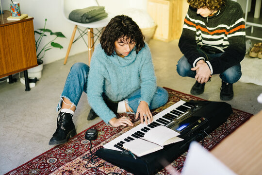 Young friends writing composition while playing synthesizer at h