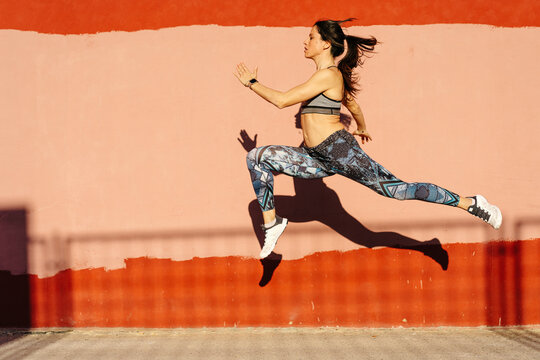 Slim sportswoman leaping against weathered wall