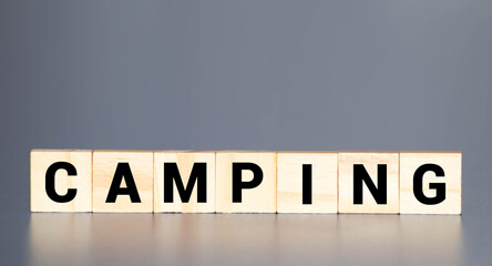 Camping word on a wooden cube sign with a blurry background of a campsite in the summer