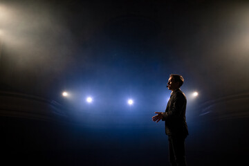 Portrait of men speaking through a microphone in dark conference hall. Man talks into microphones at press conference. Profile of young male politician speaking passionately from tribune