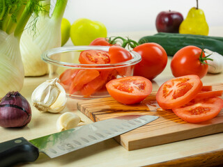 Slices of tomatoes on cutting board with sharp knife, vegetables in the glass container, still life food and cooking utensils