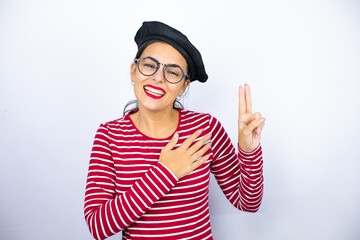 Young beautiful brunette woman wearing french beret and glasses over white background smiling swearing with hand on chest and fingers up, making a loyalty promise oath