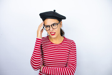 Young beautiful brunette woman wearing french beret and glasses over white background confuse and wonder about question. Uncertain with doubt, thinking with hand on head