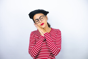 Young beautiful brunette woman wearing french beret and glasses over white background sleeping tired dreaming and posing with hands together while smiling with closed eyes.