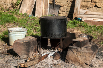 Metal pot on open fireplace in rural farm house yard in sunny day