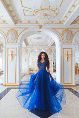 Naklejka premium Sensual brunette girl in a blue evening dress on the background of a beautiful classic interior