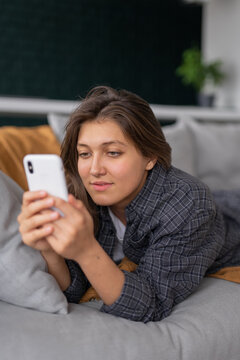 young girl lies at home on the couch and uses her phone