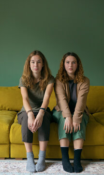two girls are equally sitting on the couch and looking at the camera