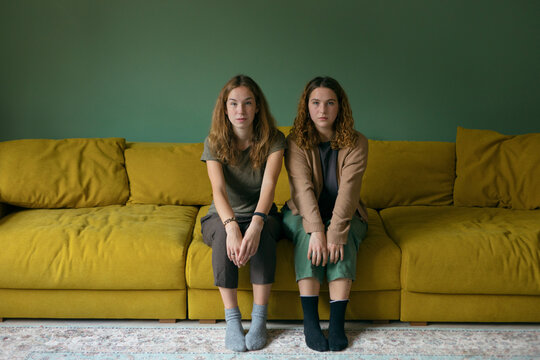 two similar girls are equally sitting on a yellow sofa