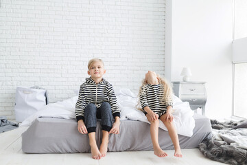 girl with white curly hair in a striped vest and a boy with blond hair in a striped vest in bedroom. Children having fun. Brother and sister. Blonde children