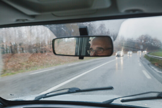 aged man driving a car on highway, reflection of eyes in mirror