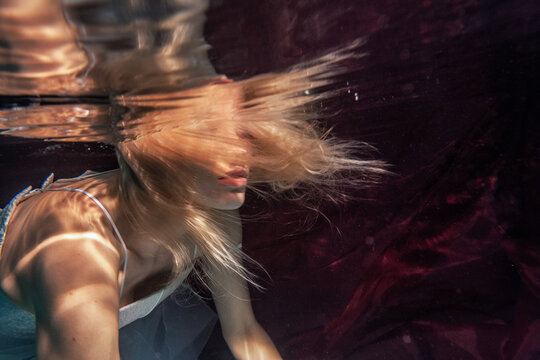 Artistic Young Woman With Long Hair Underwater On Dark Red Background