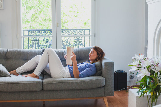 woman reading at home while lying down on the couch