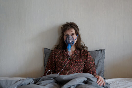 A sick woman at home alone in bed doing inhalation