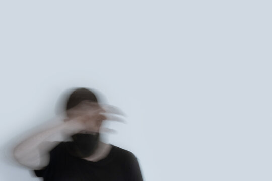 A double exposure of a man wearing a mask with his hand covering his face