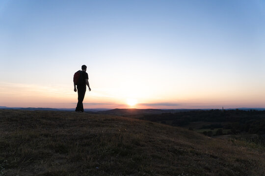 A hiker walking on top of a hill. Silhouetted against the sunset.