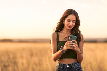Beautiful woman using mobile phone while standing on landscape against clear sky at sunset