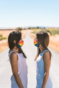 Women with rainbow face mask looking at each other while standing on road