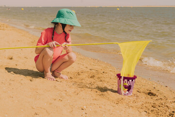 Girl with fishing net crouching at beach during sunny day