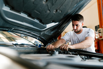 Young man repairing car while standing in auto repair shop