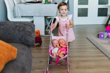 Baby girl playing with baby stroller and doll at home