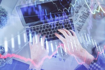 Double exposure of man's hands typing over laptop keyboard and forex chart hologram drawing. Top view. Financial markets concept.