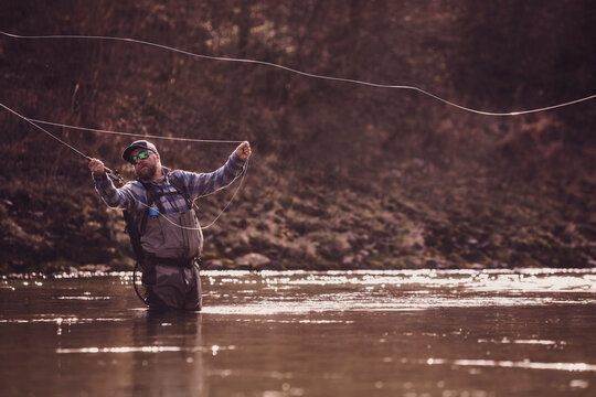 Fly fisherman throwing fishing reel in river to catch fish during sunset