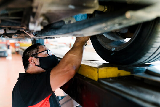 Close-up of male mechanic wearing mask examining tire in garage