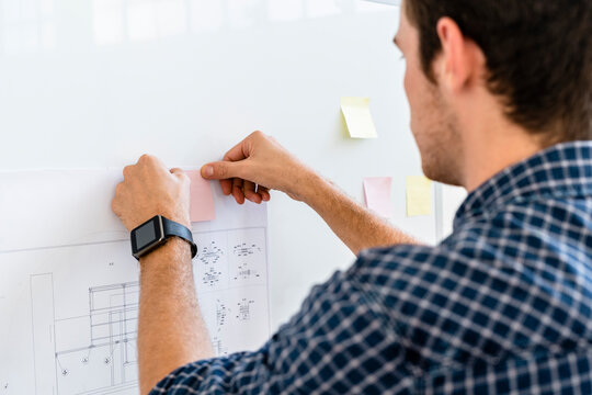 Man putting adhesive note on whiteboard while standing at office