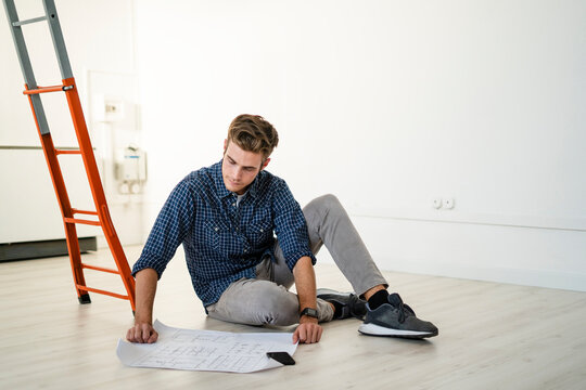 Architect sitting on floor while reading blueprint at office