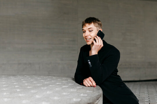 Trans Young Man Talking Over Smart Phone While Sitting At Table In Basement