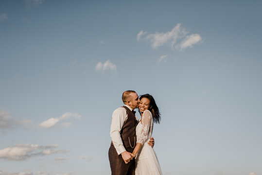 Bridegroom kissing bride on cheek during sunny day