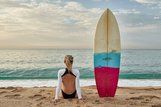Woman sitting by surfboard on sand at beach