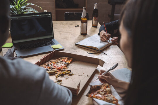 Coworkers working over coding while eating pizza at workplace
