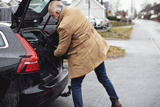 Senior man keeping golf bag in car trunk during winter