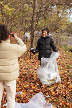 Young female environmentalist photographing smiling teenager holding microplastics in park