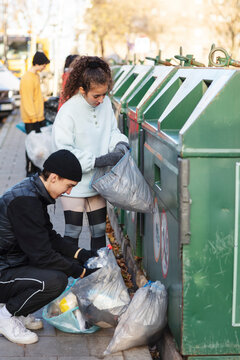 Young male and female environmentalists throwing recycling waste in garbage can