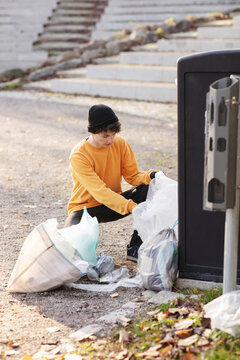 Male volunteer with plastic waste by garbage can