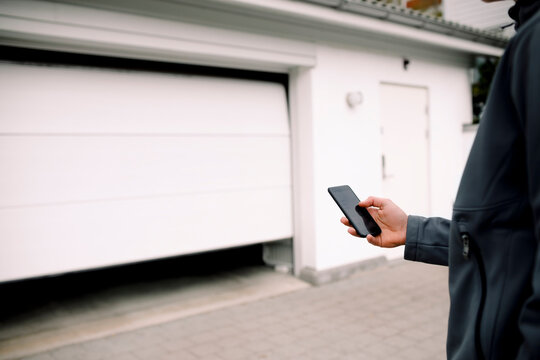 Midsection of teenage boy entering pin in smart phone while unlocking garage