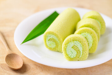 Sliced Pandan roll cake with pandan leaf on white dish and spoon on wooden table