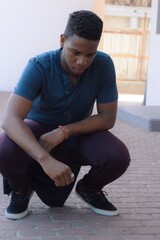 Portrait of a sad black boy squatting and facing the ground outdoor