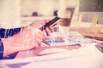 Double exposure of man's hands holding and using a phone and financial graph drawing. Analysis concept.