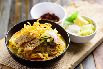 Northern Thai food (Khao Soi), Spicy curry noodles soup with beef in a bowl eating with crispy deep-fried egg noodles, pickled mustard, shallots, lime and ground chillies fried in oil