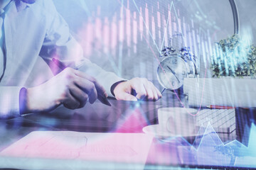 Double exposure of man's hands holding and using a phone and financial graph drawing. Analysis concept.