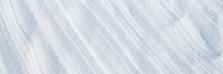 Beautiful winter background with snowy ground. Natural snow texture. Wind sculpted patterns on snow surface. Wide panoramic texture for background and design.