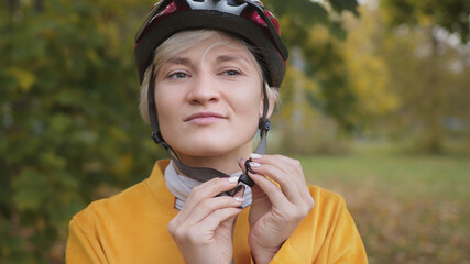 Young caucasian blond woman putting safety helmet on her head in the park. High quality photo