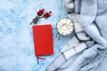 Obraz na płótnie Canvas Christmas themed top view of a red notebook, cup of marshmallow cocoa, a blanket and holiday decor items with copy space