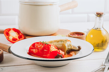 Pepper stuffed with minced chicken meat and rice in a white plate on a white wooden table.