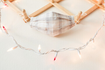 A face mask hanging on coat hanger surrounded by Christmas lights. Social Distancing this holiday season during the coronavirus pandemic.  - 388909586